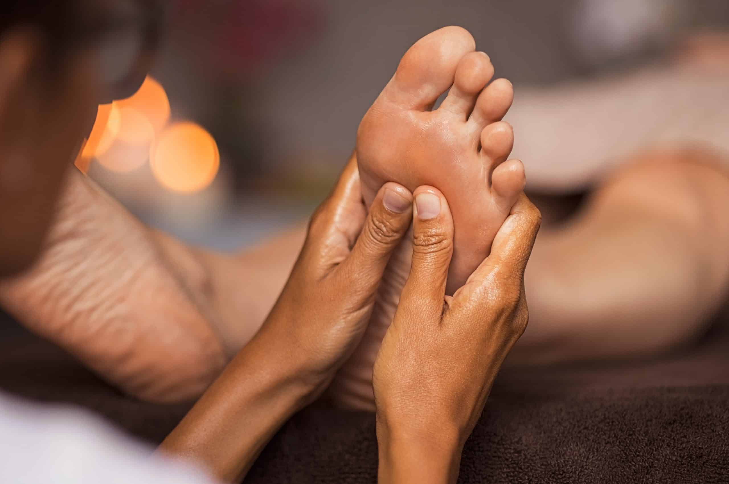 Closeup of masseuse doing foot reflexology to woman at spa. Therapist hands doing foot massage at wellness center. Woman receiving a feet massage.